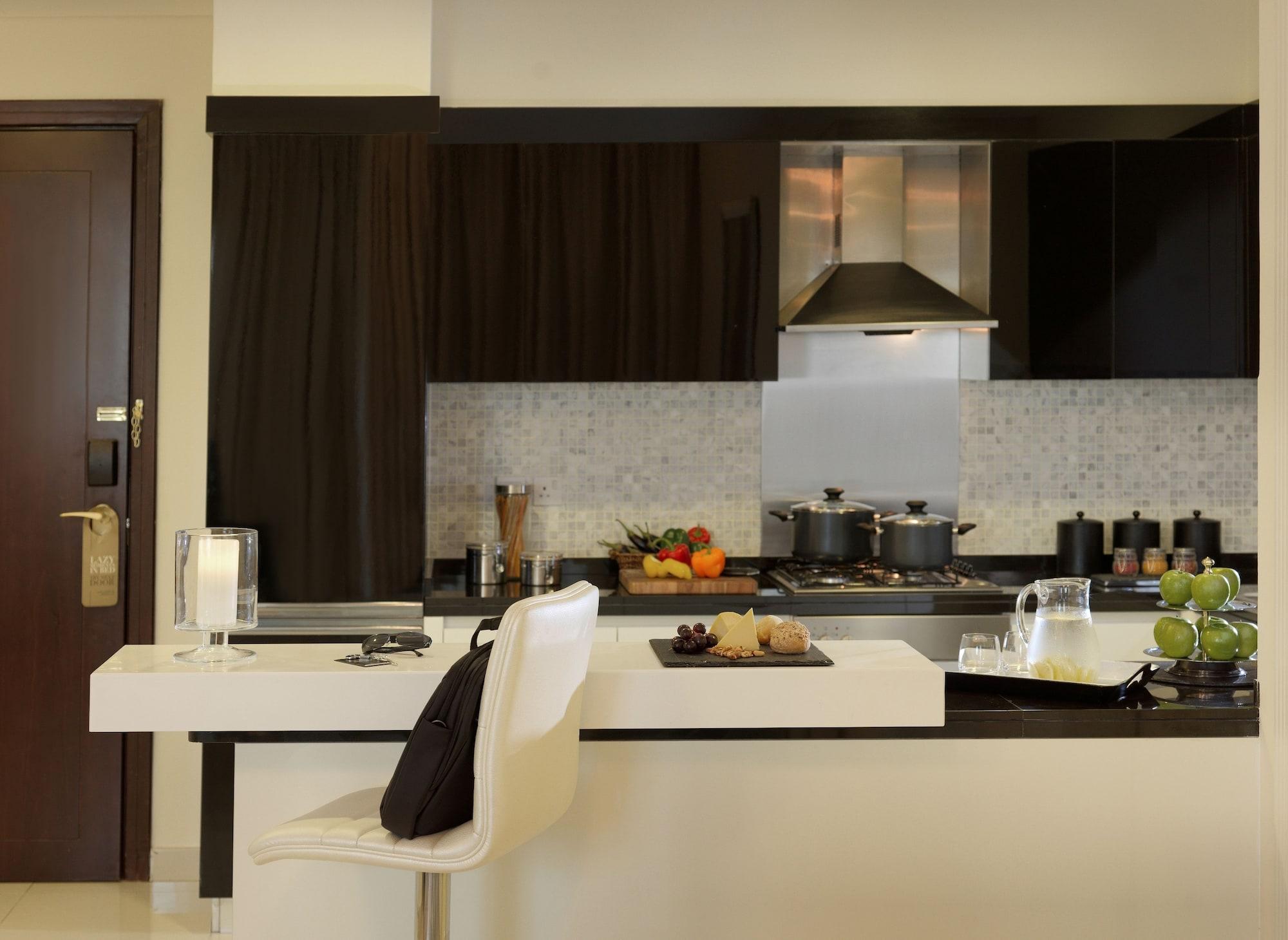 DAMAC Maison Dubai Mall Street Exterior foto The photo showcases a modern kitchen design. It features sleek black cabinetry and a light-colored countertop. There’s a stovetop with pots on it, as well as various kitchen items placed on the counter, including fruits and snacks. A kitchen island w