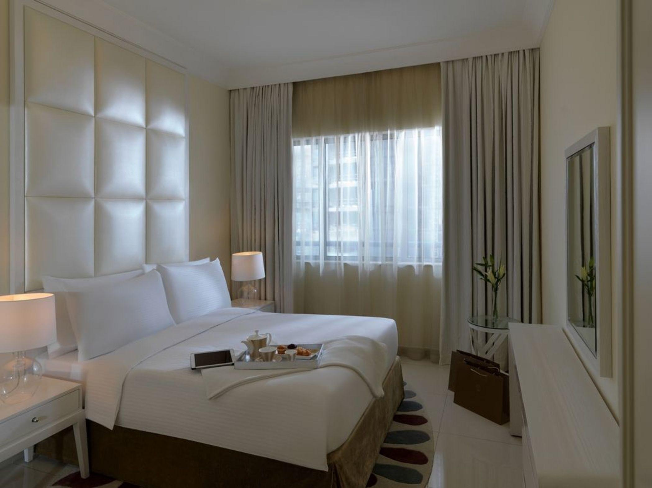 DAMAC Maison Dubai Mall Street Exterior foto The photo shows a modern hotel room. It features a large bed with white linens, complemented by soft pillows. The room has a simple yet elegant design, with light-colored walls and curtains that allow natural light to filter through. There are two be