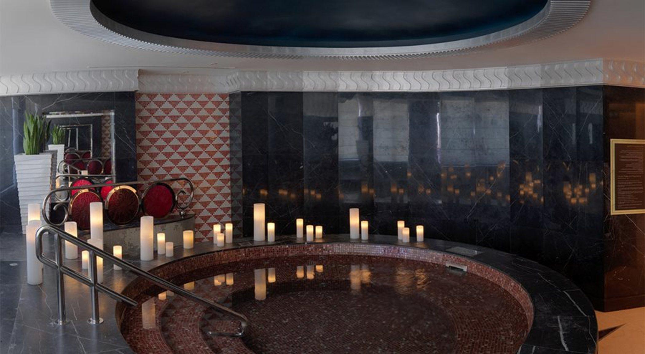 DAMAC Maison Dubai Mall Street Exterior foto The photo shows a spa-like environment featuring a round hot tub or jacuzzi. The walls are accented with dark tiles, and there is a section with a patterned design, likely decorative. Around the hot tub, there are numerous lit candles, creating a ser