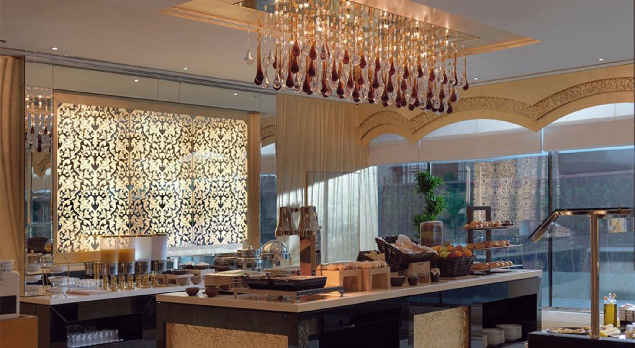 DAMAC Maison Dubai Mall Street Exterior foto The photo shows an elegantly designed dining or café area. It features a central table adorned with various food items, likely a buffet setup. Above the table, there is a striking chandelier made of glass elements that resemble elongated droplets. Th