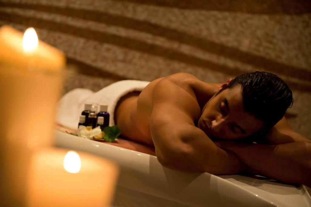 DAMAC Maison Dubai Mall Street Exterior foto The photo shows a man lying on a massage table in a spa setting. He is partially covered with a white towel, and there are a few small bottles, likely containing oils or lotions, placed nearby. Soft candlelight is visible in the foreground, creating 