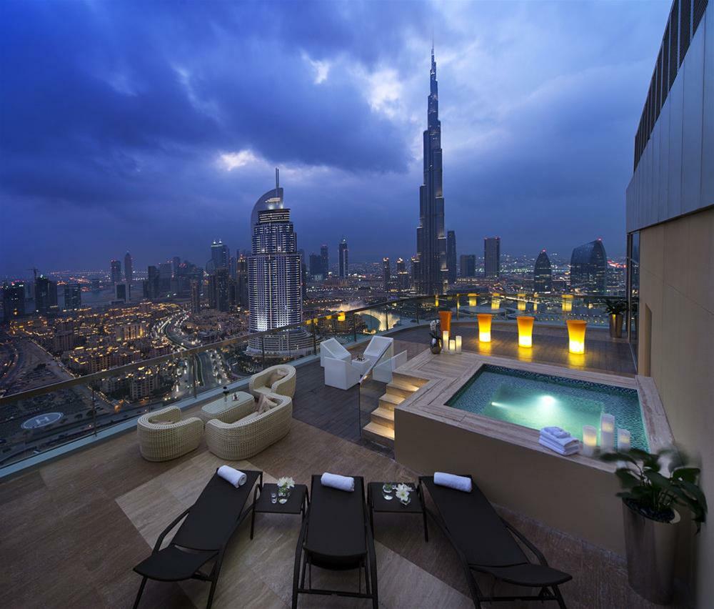 DAMAC Maison Dubai Mall Street Exterior foto The photo showcases a stylish rooftop terrace with stunning views of a cityscape at dusk. Prominent in the background is the Burj Khalifa, the tallest building in the world, standing tall against a moody sky. The terrace features luxury seating areas